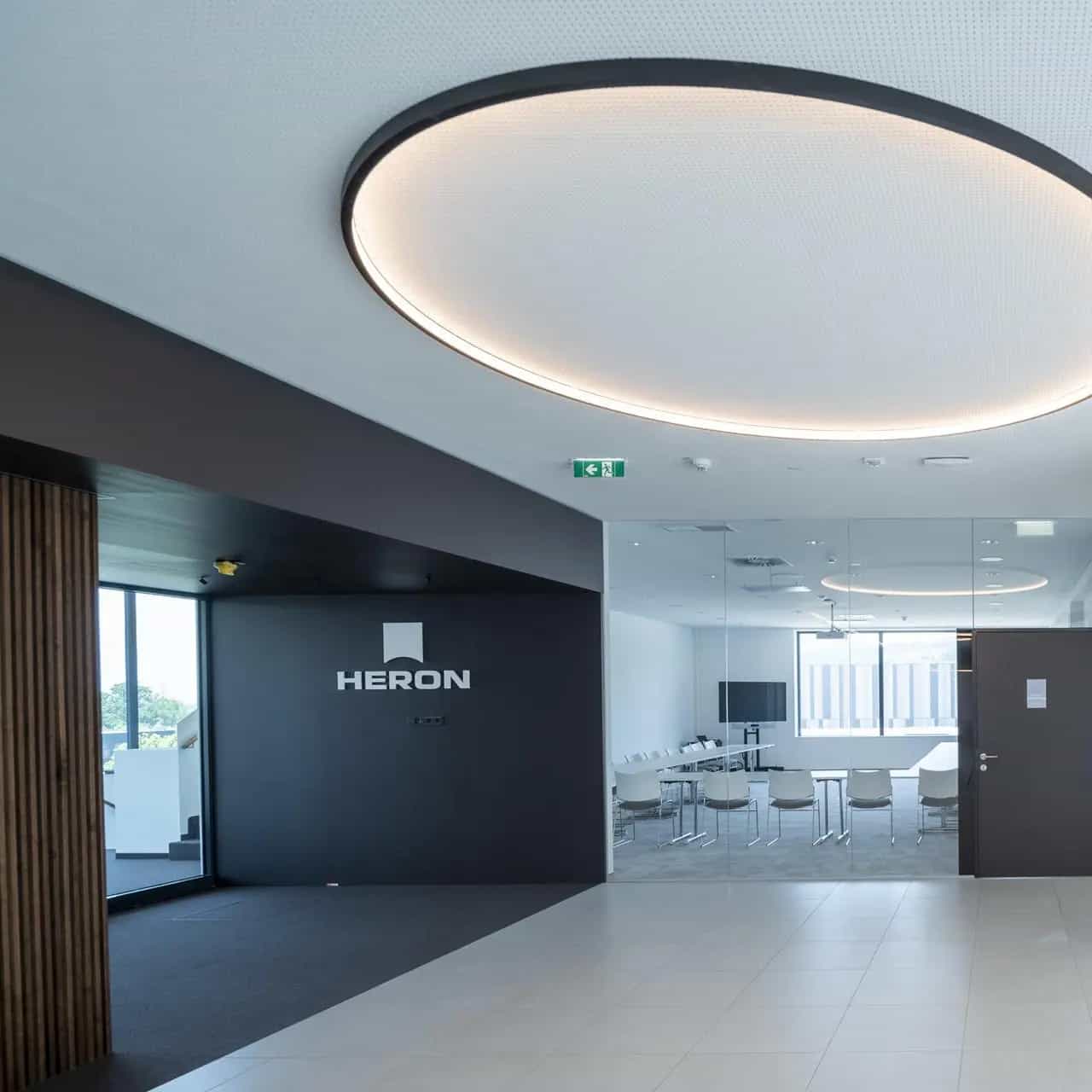 Modern office interior with glass walls, conference room and stylish lighting. HERON" logo on one wall.