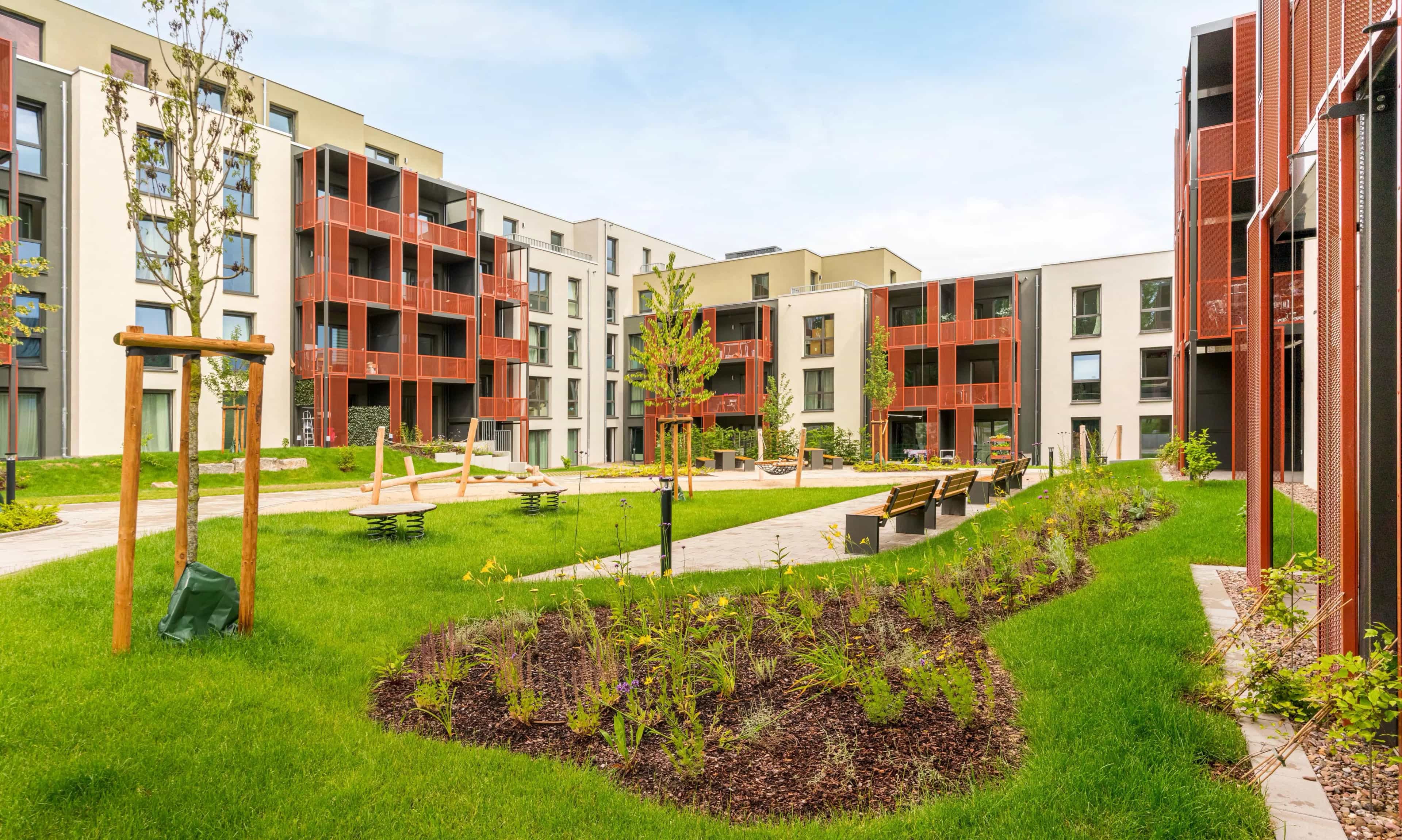 Moderner Wohnkomplex mit begrüntem Innenhof und Spielplatz, umgeben von mehrstöckigen Wohngebäuden mit Balkonen.