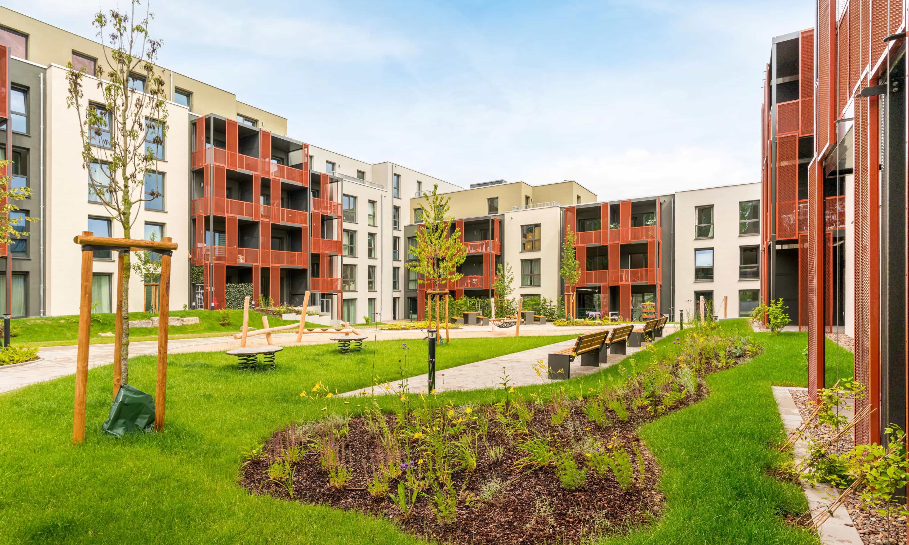 A modern residential complex with a landscaped courtyard and a playground, surrounded by multi-story apartment buildings with balconies.