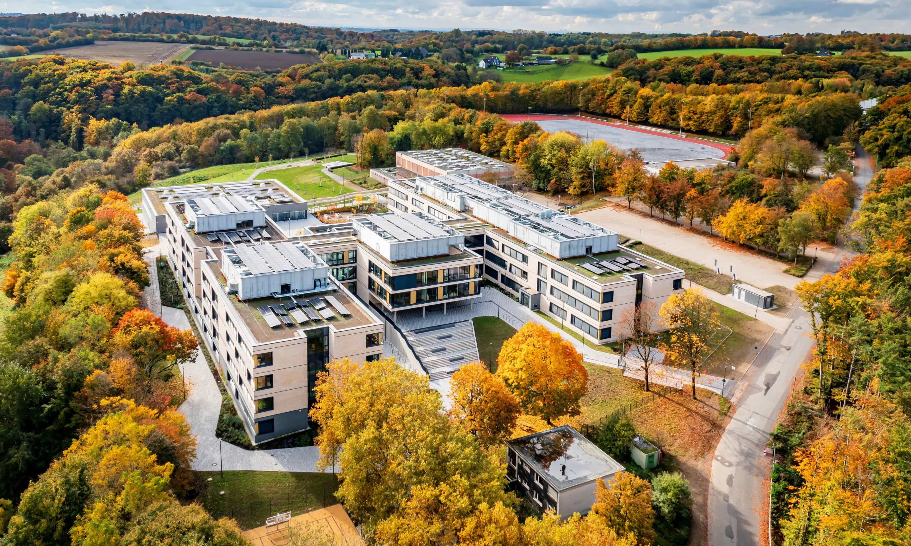 Aerial view of a modern office building in autumn, surrounded by colorful deciduous forest and green landscape.