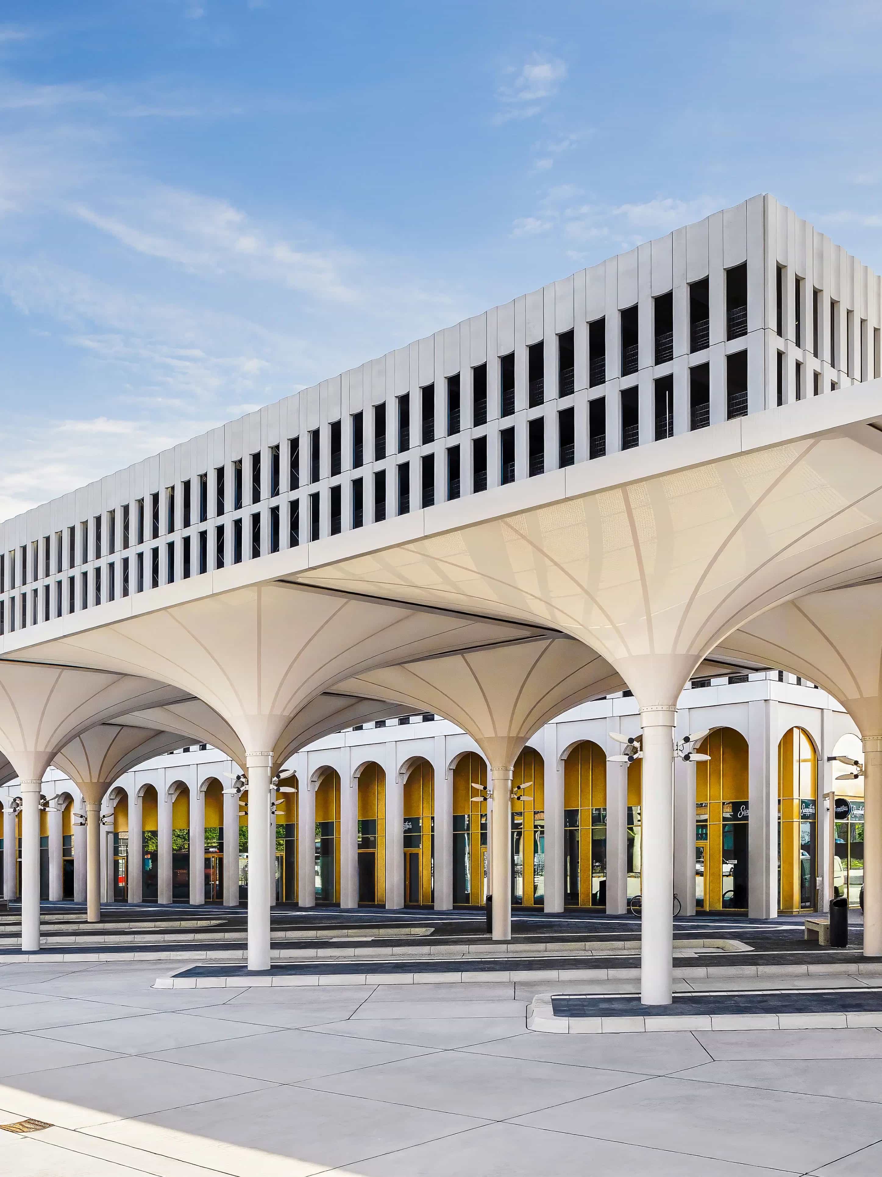 Moderne Architekturgebäude mit überdachtem Eingangsbereich und mehreren Säulen vor blauem Himmel.