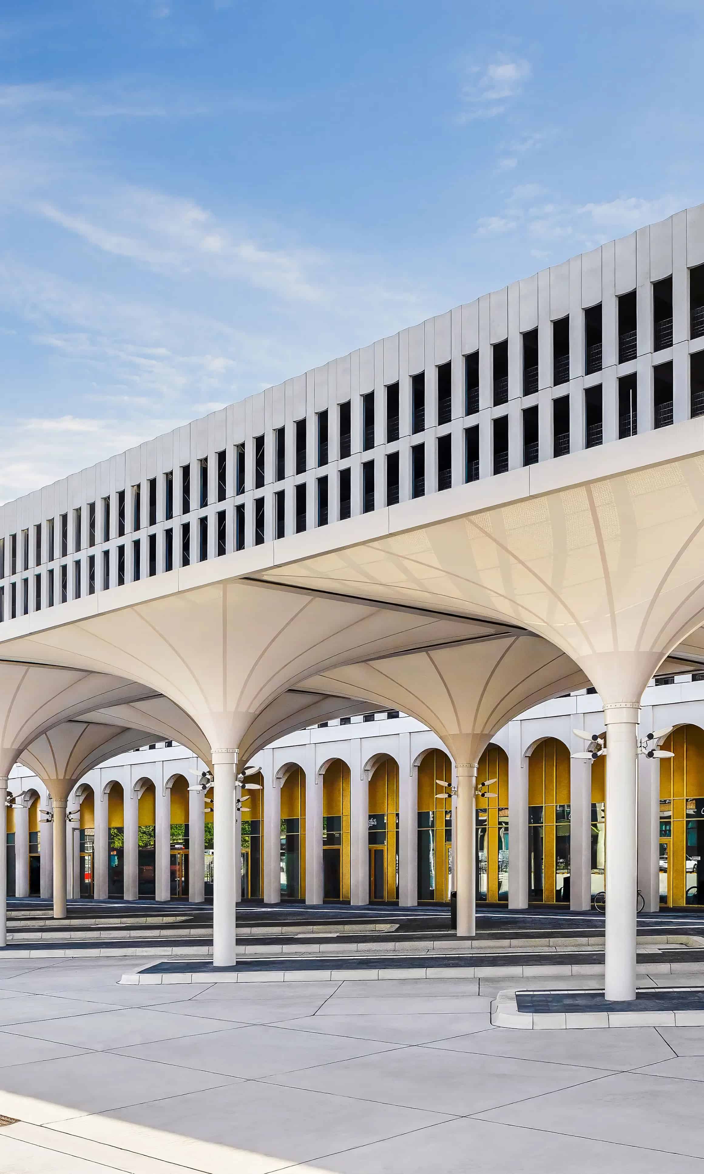 Moderne Architekturgebäude mit überdachtem Eingangsbereich und mehreren Säulen vor blauem Himmel.